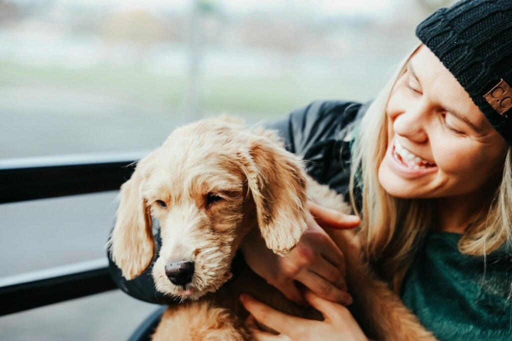 smiling woman wearing gray jacket carrying beige Labradoodle